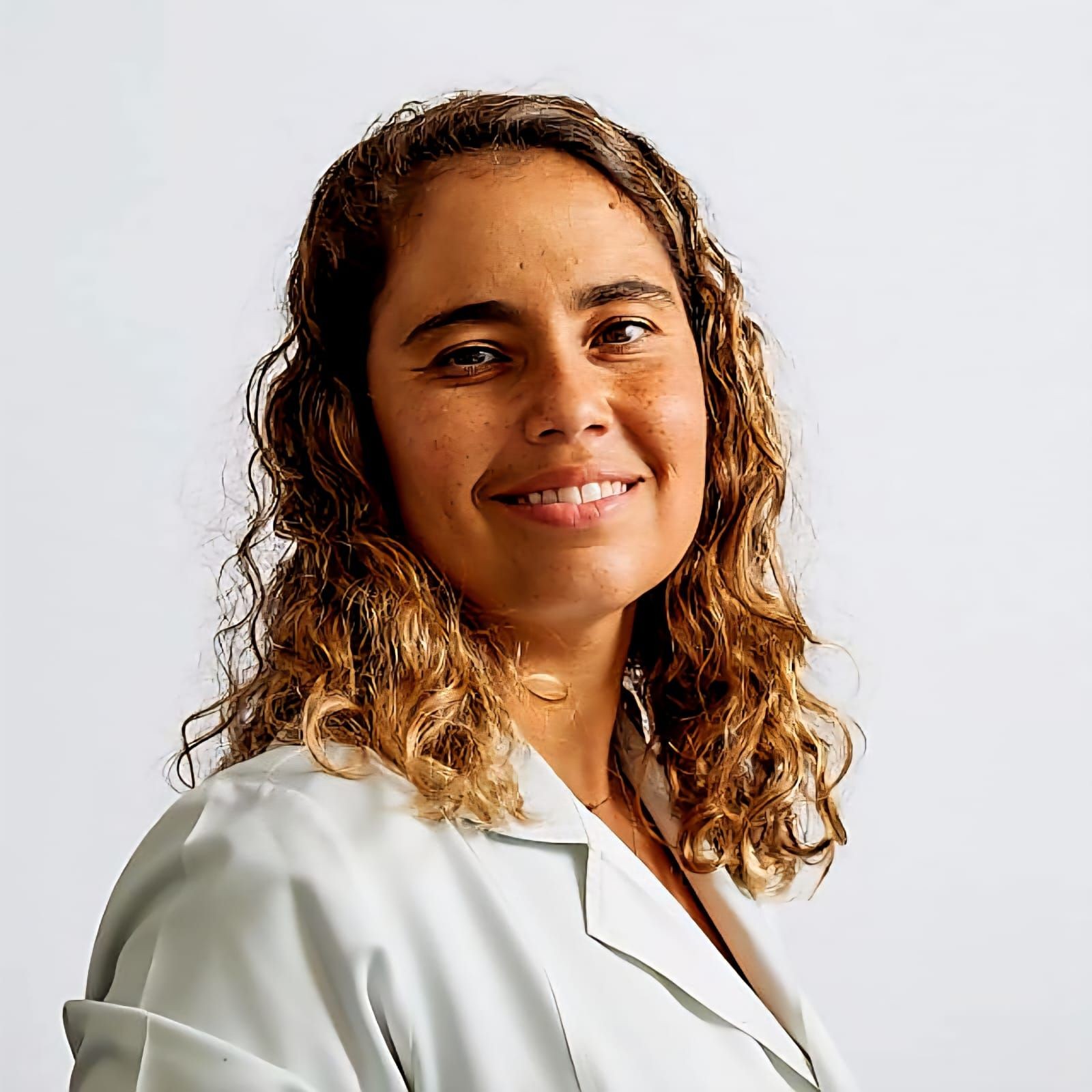 Person with curly brown hair wearing a white lab coat, standing against a plain background.